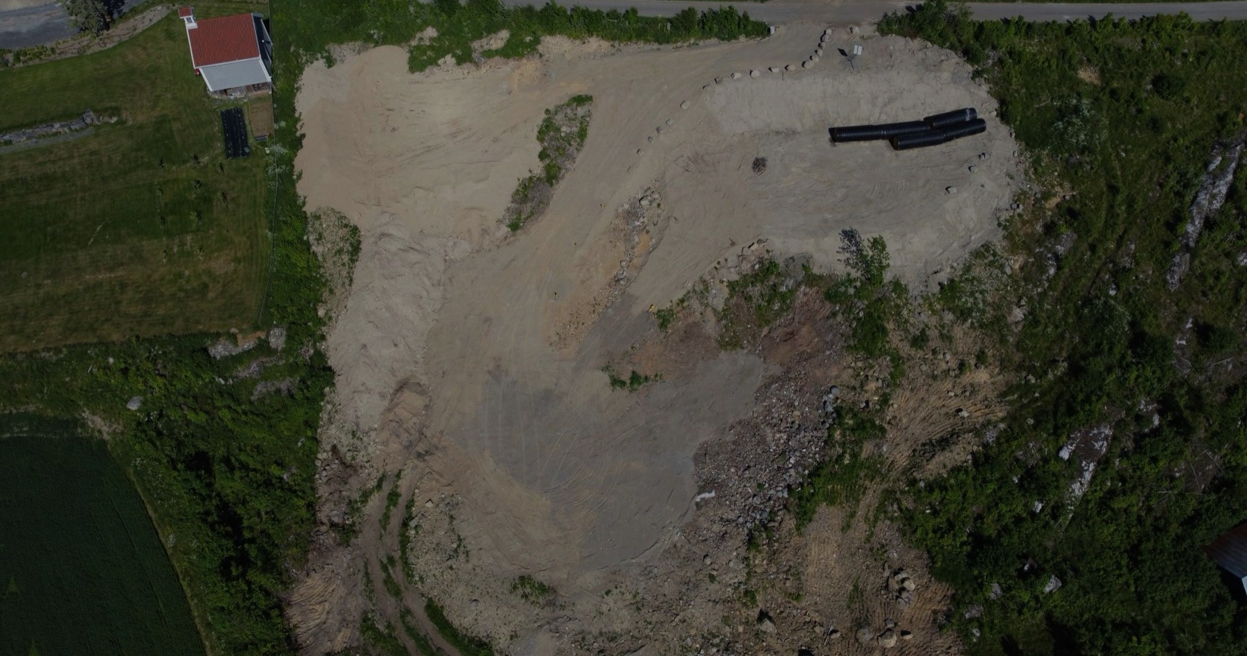Dronebilde av deponiet til Innlandet Miljøpark: planert grus og steinmasser omgitt av skog og jorder